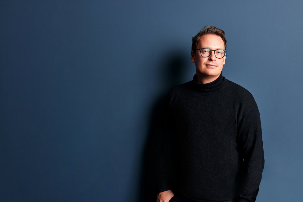 Finn Hänsel, Gründer und MD Sanity Group, vor einer dunkelblauen Wand.