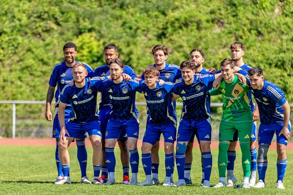 Elf Fußballspieler in blauen Trikots posieren gemeinsam auf einem Spielfeld vor einem Spiel