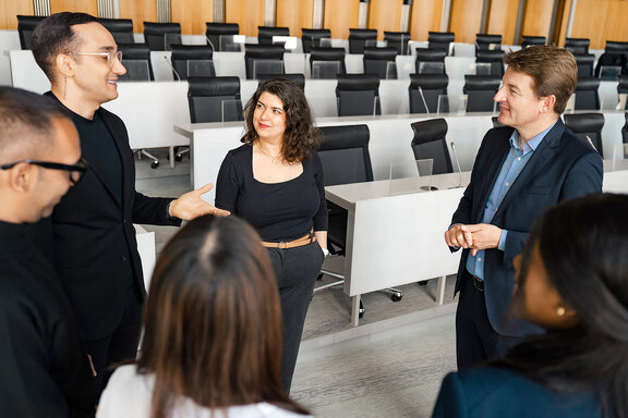 Professor steht mit zwei Studentinnen und zwei Studenten im Gespräch in einem Hörsaal