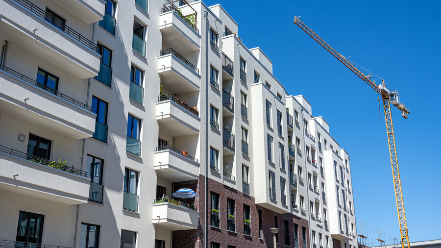 Zu sehen ist ein Kran neben einem Mehrfamilienhaus mit Wohnungen und Balkon.
