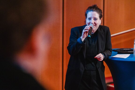 Eine Frau spricht an einem Stehtisch in ein Mikrofon.