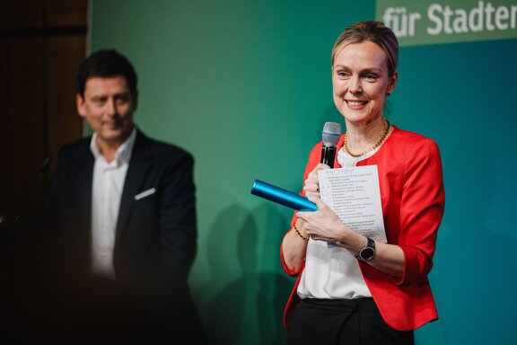 IHK-Hauptgeschäftsführerin Manja Schreiner steht mit Mikrofon auf einer Bühne, neben ihr ein Mann.