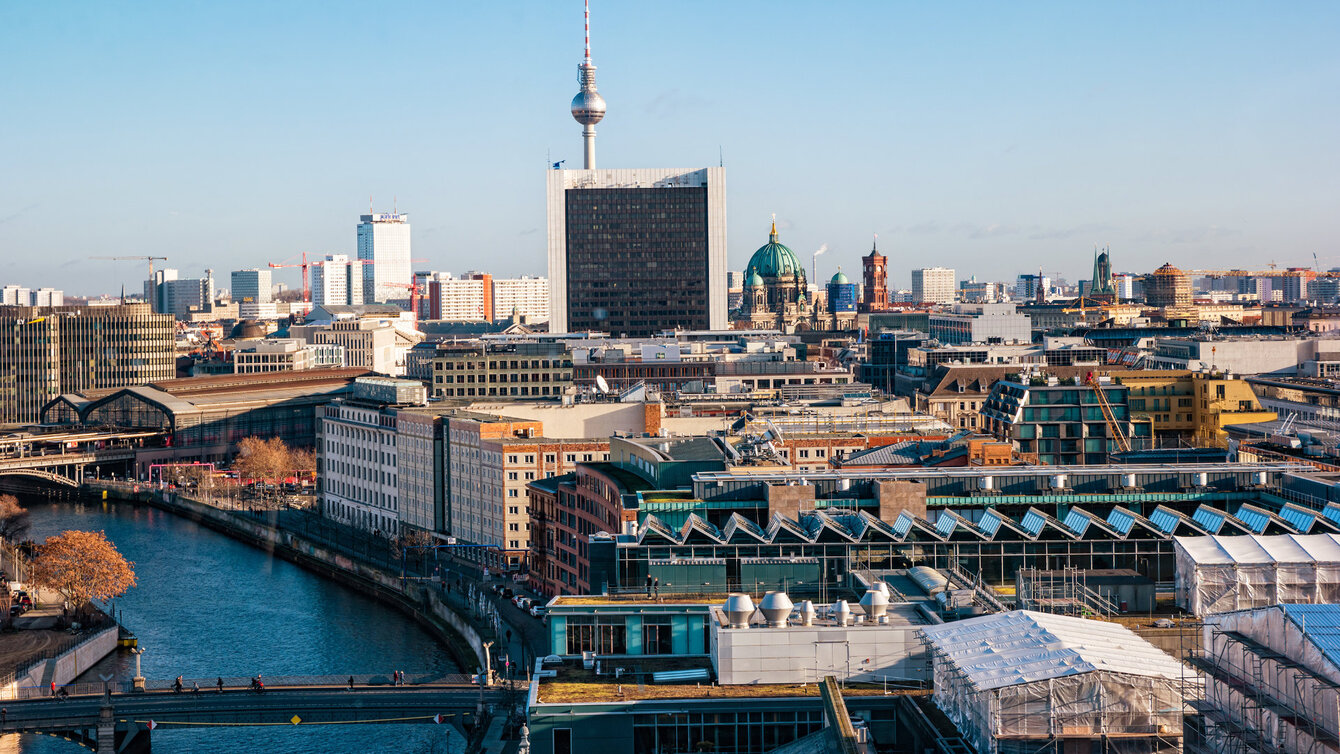 Panorama von Berlin-Mitte bei blauem Himmel mit dem Fernsehturm in der Bildmitte, dem Berliner Dom und dem Roten Rathaus, links die Spree und der Bahnhof Friedrichstraße.