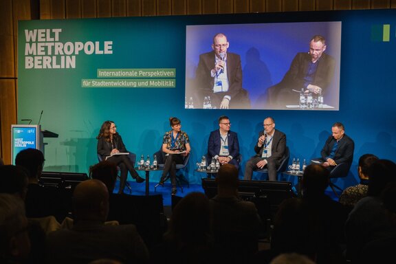 Fünf Personen unterhalten sich sitzend auf einer Bühne vor Publikum.