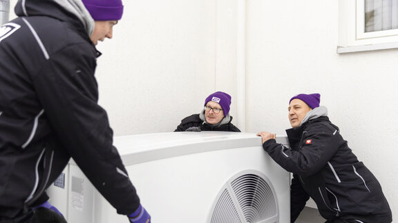 Drei Männer tragen eine Wärmepumpe – das Bild symbolisiert das Thema Mitarbeitergewinnung.