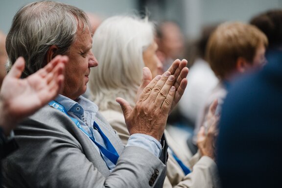Zu sehen ist ein im Publikum sitzender Mann, der applaudiert.