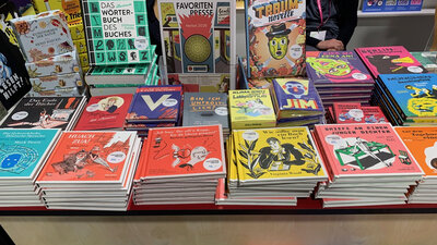 Mehrere bunte Bücher liegen ausgelegt auf einer Verkaufsfläche.