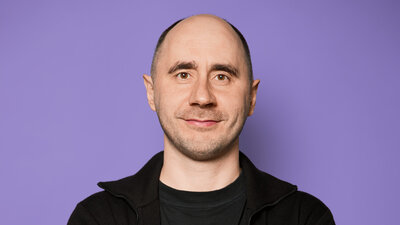 Ein Mann posiert freundlich lächelnd und mit verschränkten Armen für ein Foto: Es ist der Co-Founder von Vivid, Alexander Emeshev.