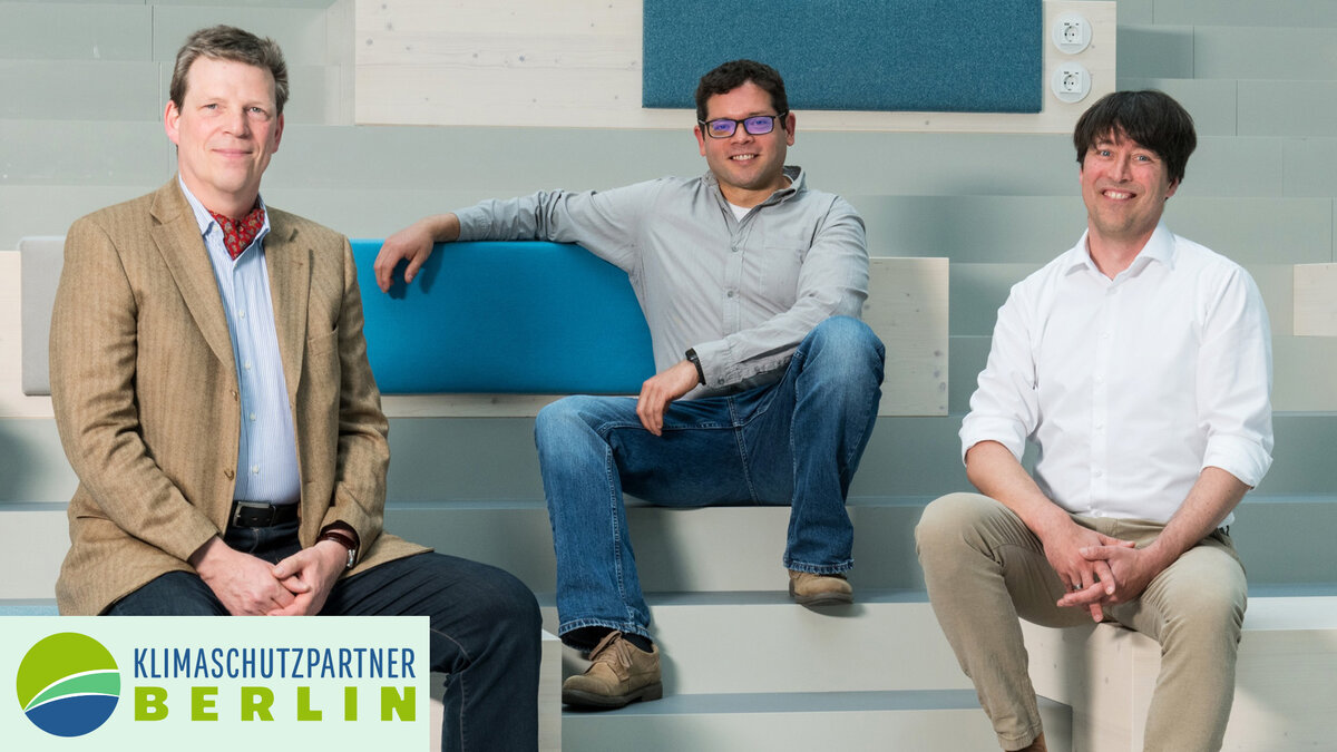 Drei Männer sitzen auf einer hellblauen Treppe und schauen freundlich in die Kamera. 