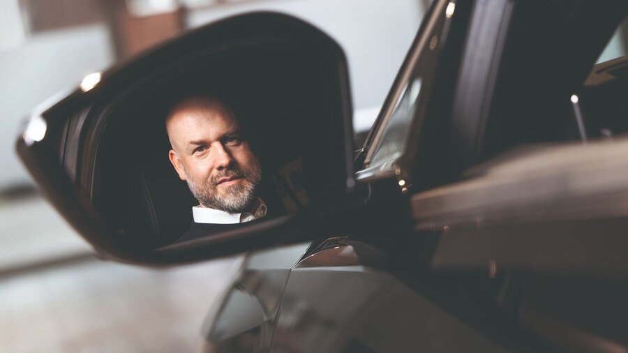 Das Foto zeigt Michael Fischer, Abteilungsleiter Public & Governmental Affairs bei Miles. Sein Spiegelbild ist im Außenspiegel eines Autos zu sehen.