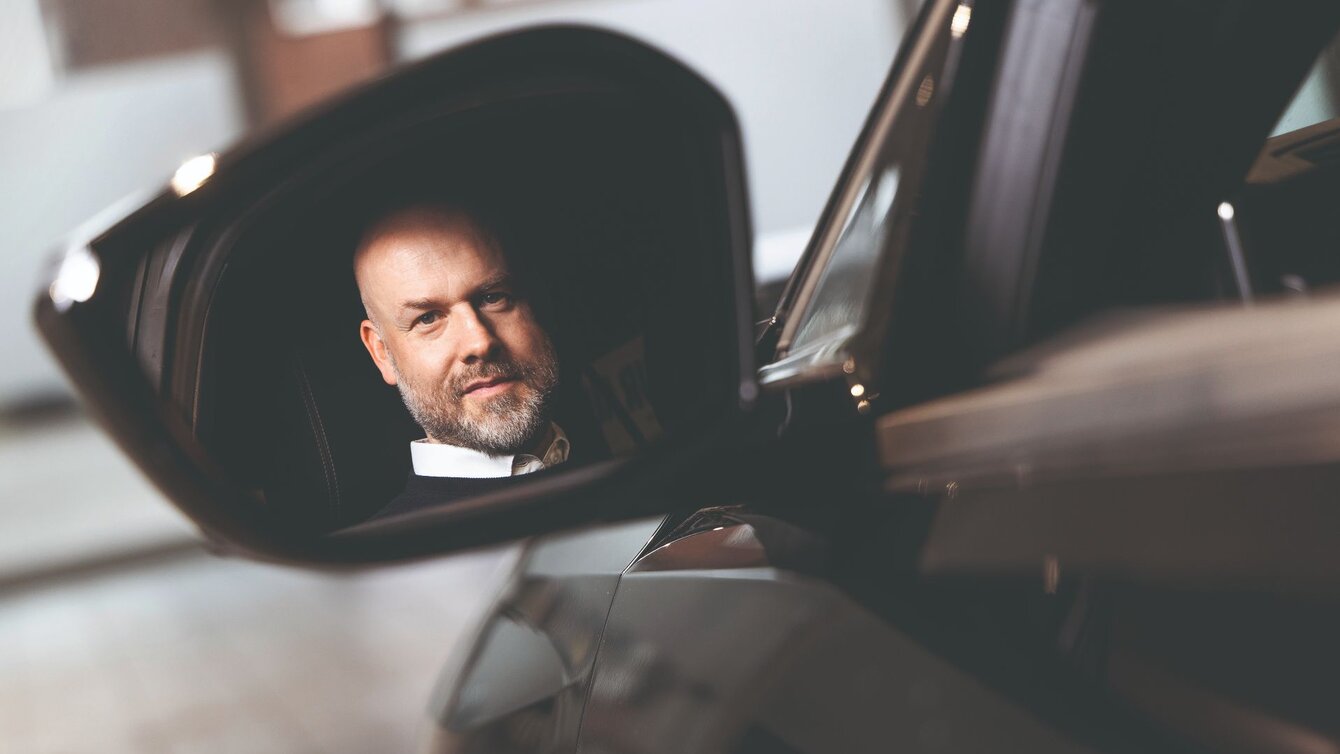Das Foto zeigt Michael Fischer, Abteilungsleiter Public & Governmental Affairs bei Miles. Sein Spiegelbild ist im Außenspiegel eines Autos zu sehen.