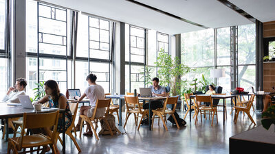 Blick in den Innospace des betahaus Kreuzberg. Menschen sitzen an mehreren Tischen. Große Fensterfronten.