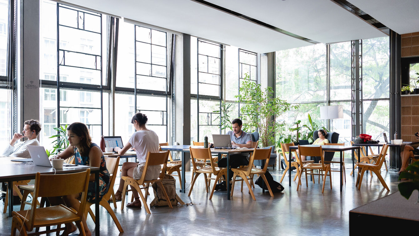 Blick in den Innospace des betahaus Kreuzberg. Menschen sitzen an mehreren Tischen. Große Fensterfronten.