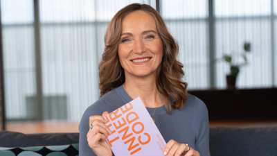 Zu sehen ist eine mittelalte blonde Frau, die freundlich in die Kamera blickt und das Buch The Inner Code in der Hand hält.