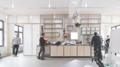 Innenraum eines hellen, modernen Workspaces, in dem mehrere Menschen stehend arbeiten. 