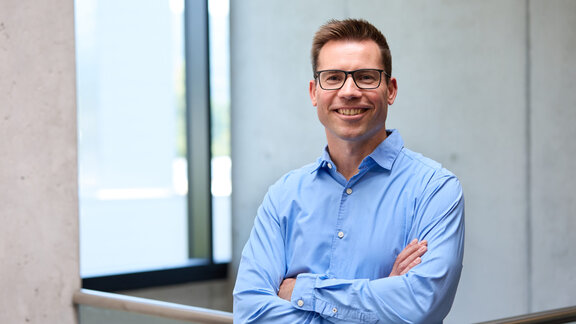 Ein Mann in einem hellblauen Hemd lächelt freundlich in die Kamera. 