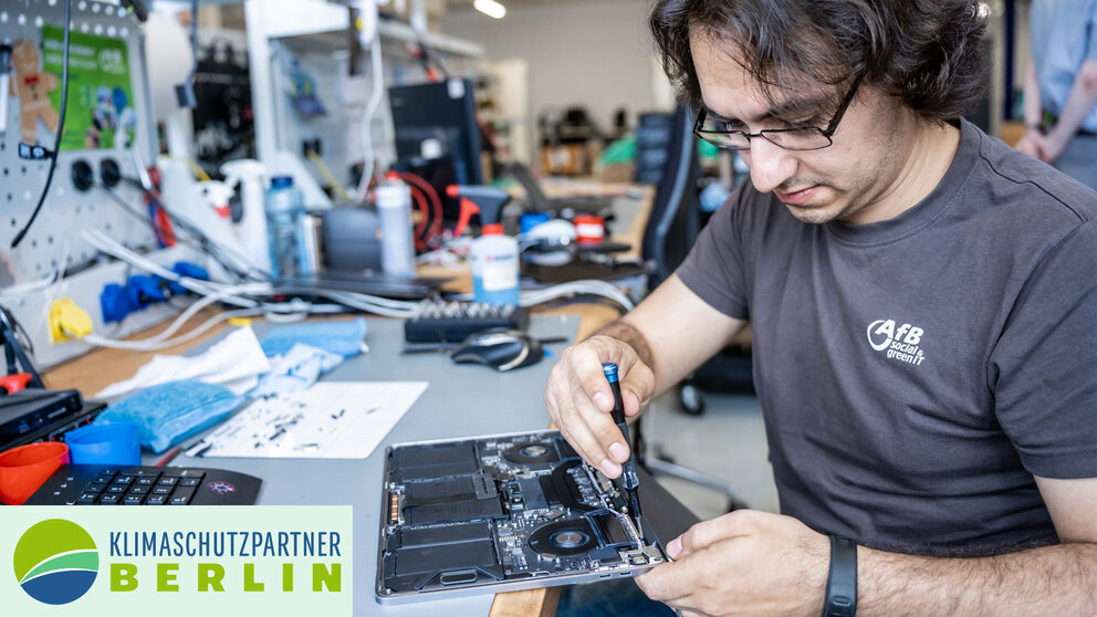 Ein Mann sitzt an einem Schreibtisch und repariert einen Laptop. 