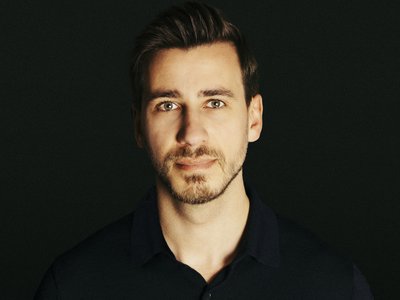 Porträt eines Mannes vor einem schwarzem Hintergrund.