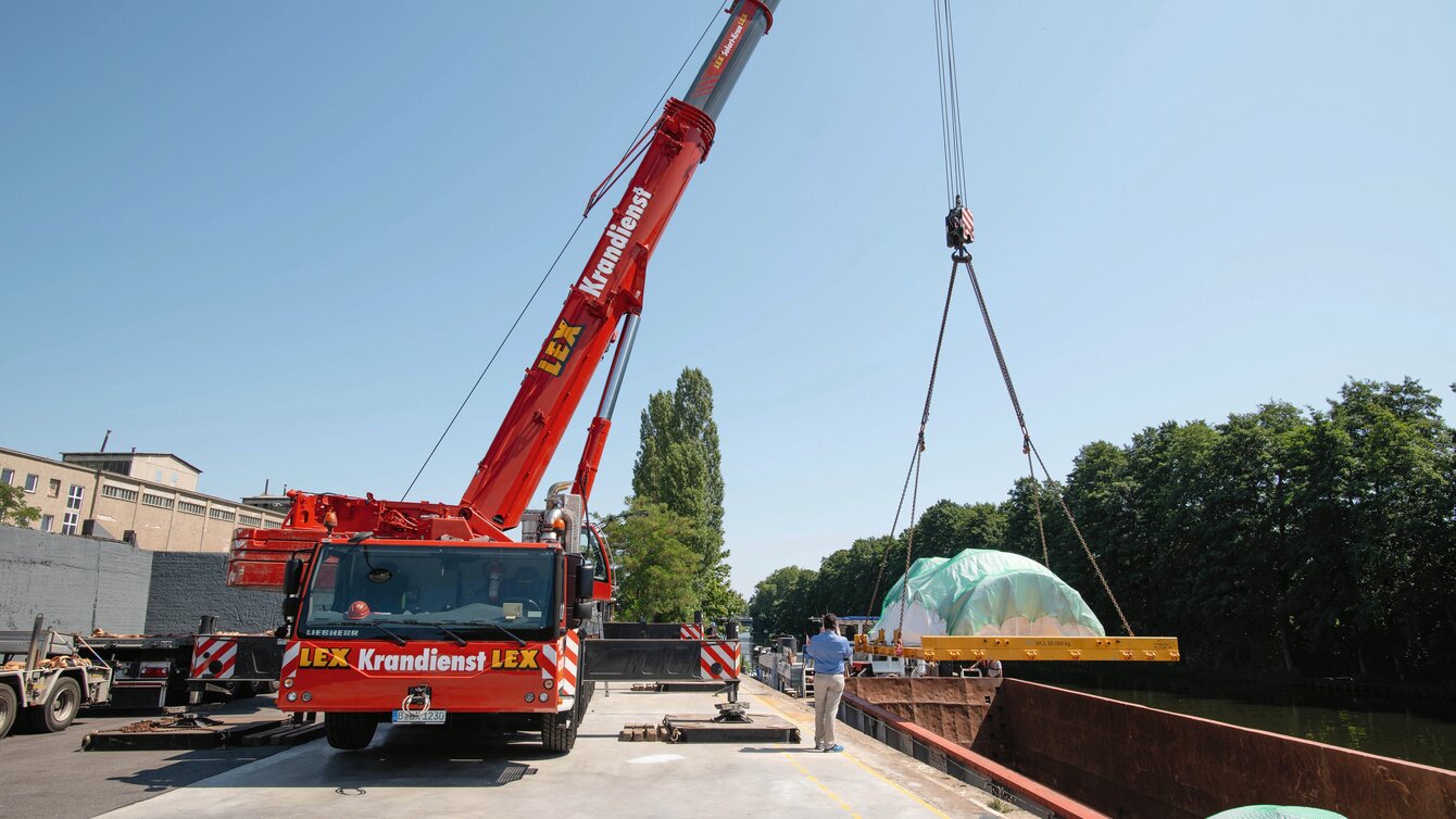Zu sehen ist ein Lkw-Kran, der Ladung auf einem Wasser-Umschlagplatz verlädt.