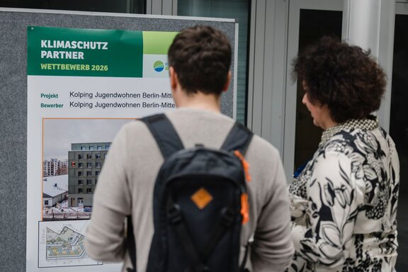Zu sehen sind zwei Personen von hinten, die sich eine Infotafel ansehen.