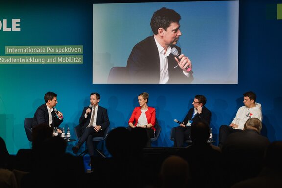 Fünf Personen unterhalten sich sitzend auf einer Bühne vor Publikum.