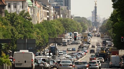 Zu sehen ist eine vielbefahrene Hauptstraße in einer Großstadt. Im Hintergrund ist die Siegessäule in Berlin zu erkennen.