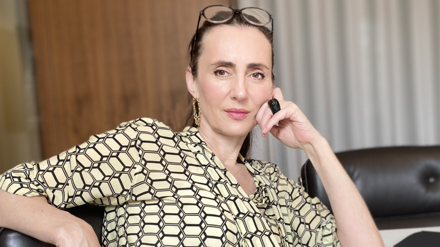 Zu sehen ist eine Frau in einem gemusterten Hemd, mit einer Lesebrille auf dem Kopf. Sie schaut neutral in die Kamera.