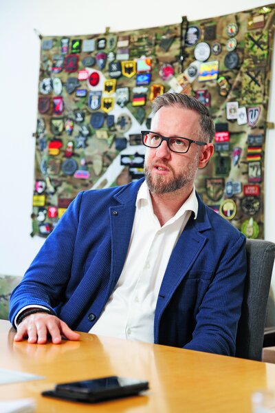 Sebastian Stutte im Interview und sitzt vor einem bunten Gemälde an einem Holztisch