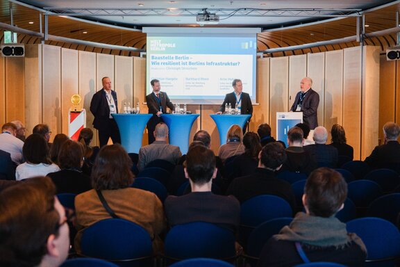 Vier Personen unterhalten sich auf einer Bühne vor Publikum.