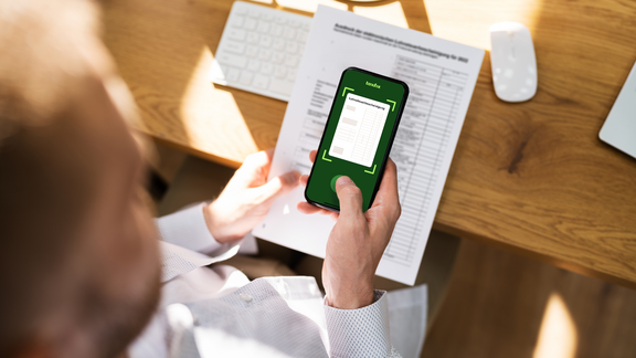 Ein Mann fotografiert seine Lohnsteuerbescheinigung mit der Taxfix-App auf seinem Smartphone ab