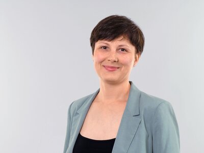 Zu sehen ist eine mittelalte Frau mit kurzen braunen Haaren, die freundlich in die Kamera blickt.