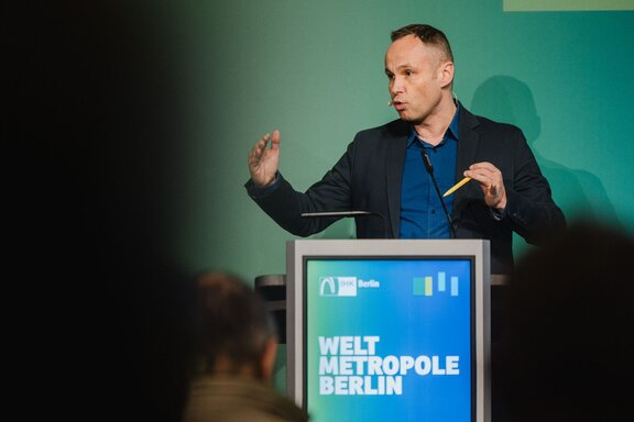 Ein Mann hält vor Publikum eine Rede an einem Pult und gestikuliert.