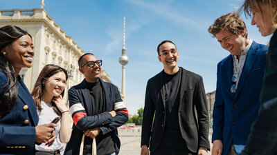 Sechs junge Menschen stehen im Halbkreis zusammen. Sie lächeln sich freundlich an.