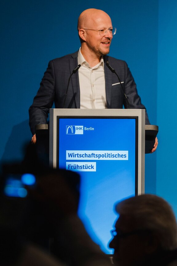 Zu sehen ist ein mittelalter Mann mit Brille und Glatze im Anzug. Er steht an einem Redepult - es handelt sich um den IHK-Präsidenten Sebastian Stietzel.