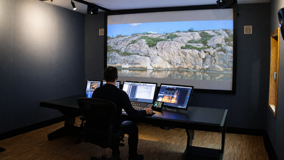 Ein Mann sitzt vor drei Bildschirmen in einem Film Ton-Studio