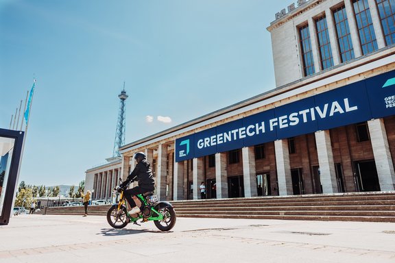 Person fährt E-Bike vor dem Palais de Tokyo mit Banner 'Greentech Festival' in Berlin