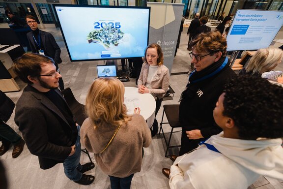 Man blickt von oben auf einen Stehtisch, um den fünf Personen stehen und sich unterhalten.