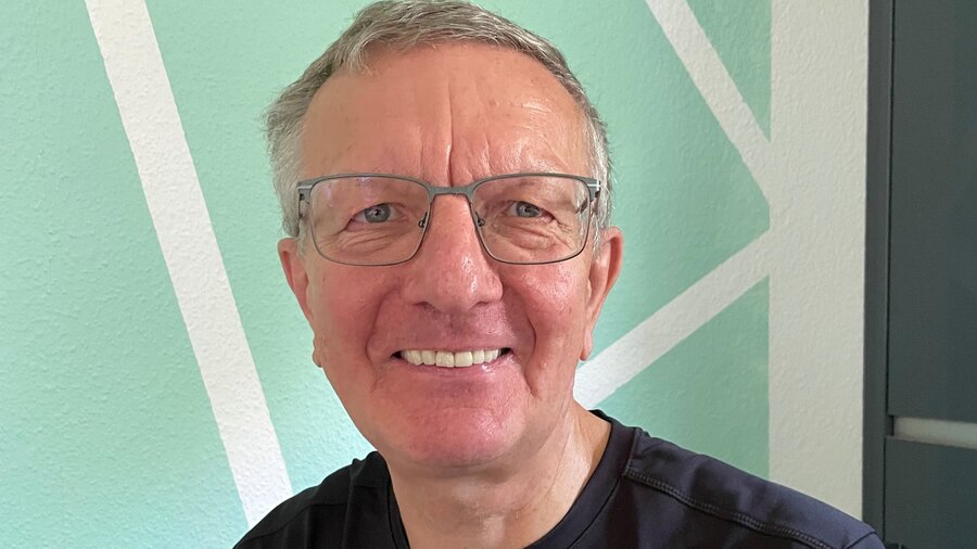 Auf dem Bild ist ein älterer Mann mit Brille zu sehen, der in die Kamera lächelt.