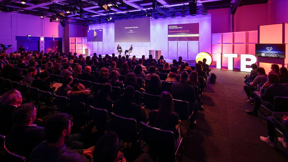 Ein Konferenzraum mit voll besetzten Stuhlreihen und zwei Personen, die auf dem Podium diskutieren