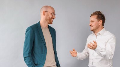 Zu sehen sind zwei mittelalte Männer im Gespräch.