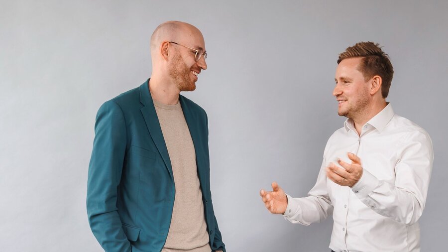 Zu sehen sind zwei mittelalte Männer im Gespräch.