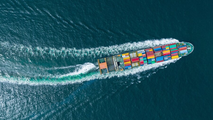 Zu sehen ist ein Containerschiff, welches von oben im Meer fotografiert wurde.