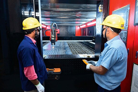 Zwei Männer in gelben Bauhelmen arbeiten an einer Schweißmaschine