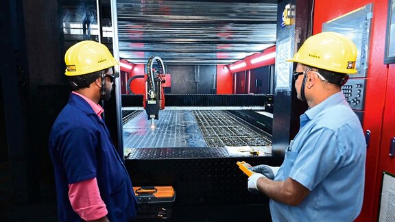 Zwei Männer in gelben Bauhelmen arbeiten an einer Schweißmaschine