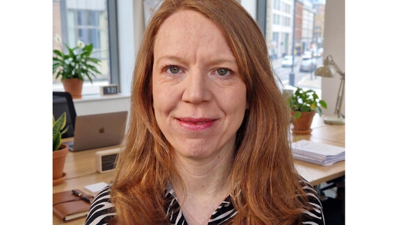Annalena Bredehoeft-Crowley sitzt vor einem Schreibtisch und Fenstern.