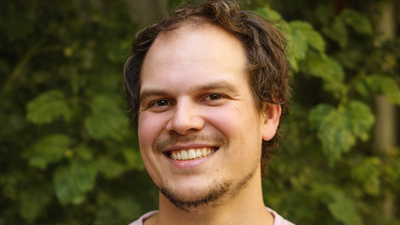 Ein mittelalter Mann in einem rosa Shirt steht lächelnd vior einer Hecke. Es ist Johannes Kunz, Gründer von FSL Sound Lab