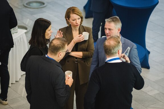 Man sieht eine Gruppe aus fünf Personen, zwei Frauen und drei Männer, die sich stehend im Kreis unterhalten. Sie befinden sich auf der Digital-Konferenz der IHK Berlin und HTW Berlin.