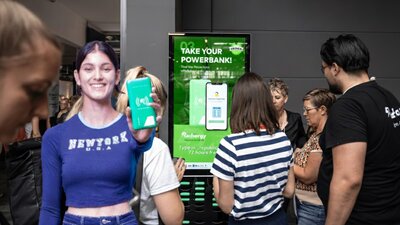 Auf dem Bild sind Menschen zu sehen, die vor einer Powerbank-Station stehen.