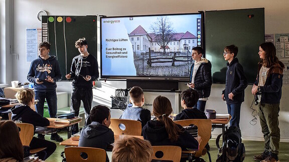 Fünf Schüler halten einen Vortrag in einem Klassenzimmer. 