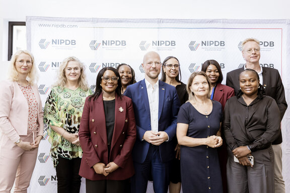 Eine Gruppe von neun Personen steht vor einer Fotowand mit dem Logo des Namibia Investment Promotion and Development Board (NIPDB). Die Personen stehen eng nebeneinander und blicken in Richtung Kamera.“